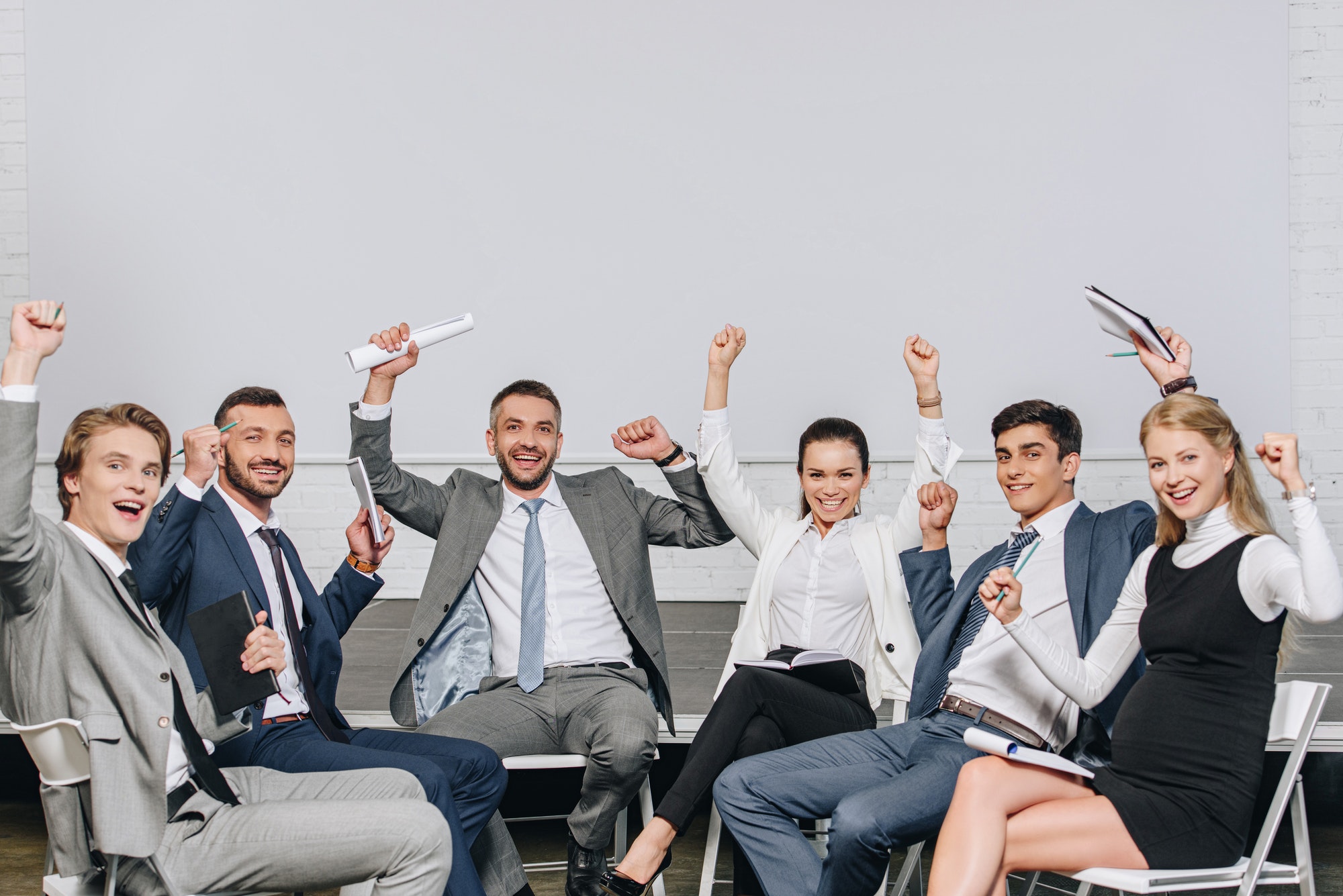 happy businesspeople with raised hands sitting on chairs at training in hub